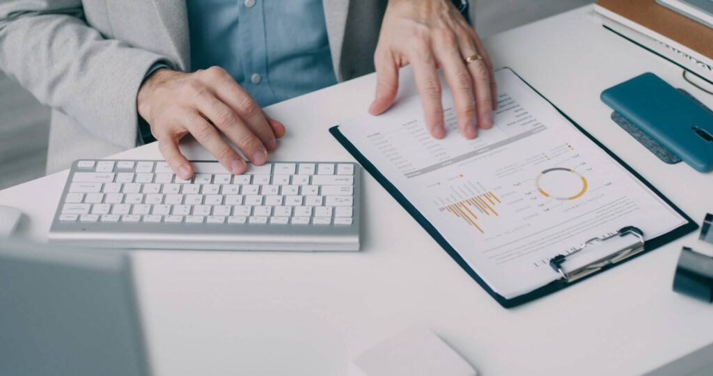 Persona usando un teclado y revisando una hoja con datos